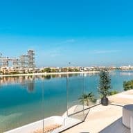 Moderne Balkonansicht mit eleganter Glasgeländer, die auf eine ruhige Wasserfront und markante, futuristische Gebäude unter einem klaren blauen Himmel blickt.