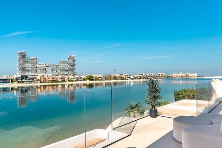 Modern balcony view with sleek glass railing overlooking a calm waterfront and distinctive, futuristic buildings under a clear blue sky.