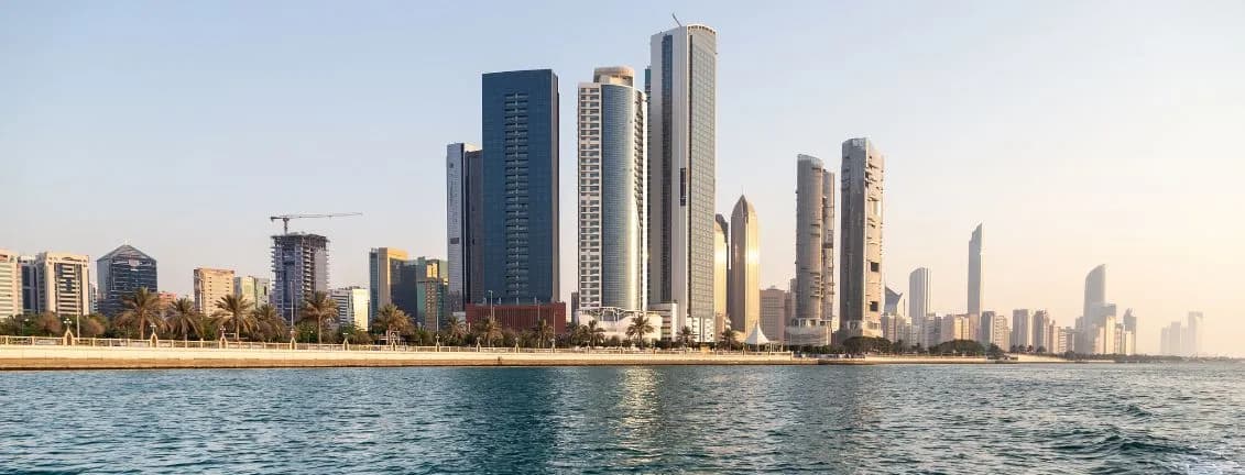 Skyline of Abu Dhabi with modern skyscrapers along the waterfront, viewed from the water under a clear sky.
