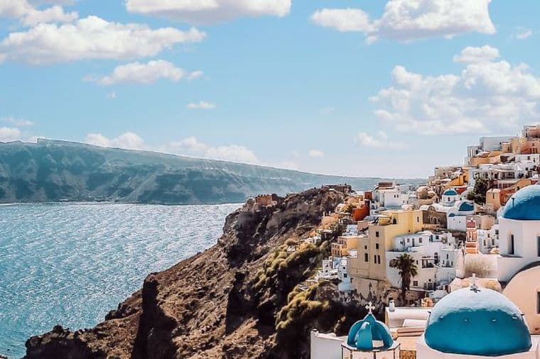 Panoramic view of Santorini with whitewashed buildings, blue-domed churches, and the Aegean Sea.