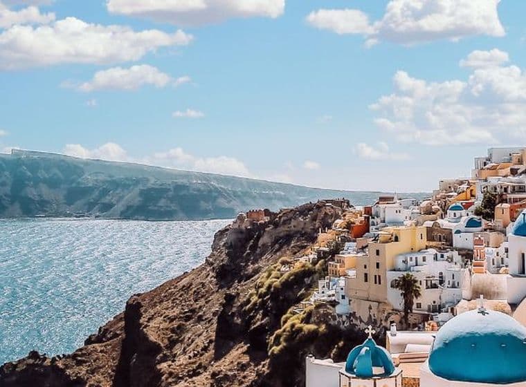 Panoramic view of Santorini with whitewashed buildings, blue-domed churches, and the Aegean Sea.