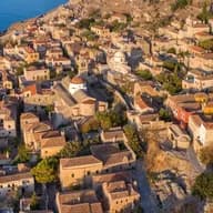 Aerial view of the medieval stone castle town of Monemvasia with brown-tiled roofs overlooking the deep blue sea.