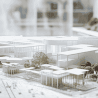 In einem Planungsbüro nehmen Hände ein maßstabsgetreues Architekturmodell auf Bauplänen in die Hand, auf denen moderne weiße Gebäude und Bäume zu sehen sind