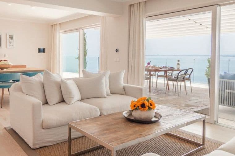 Bright open-plan living room with elegant contemporary furnishings, floor-to-ceiling sliding doors, and panoramic sea views