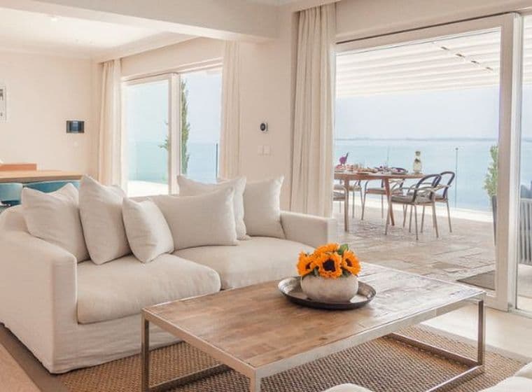 Bright open-plan living room with elegant contemporary furnishings, floor-to-ceiling sliding doors, and panoramic sea views