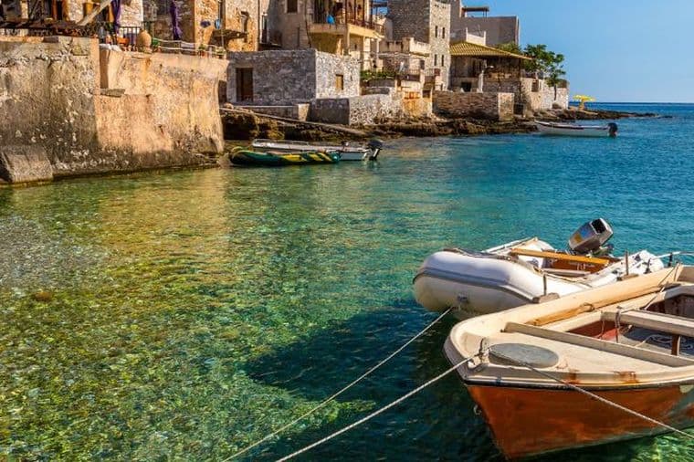 Traditional seaside village with crystal-clear turquoise waters, stone architecture, and small boats along the coast
