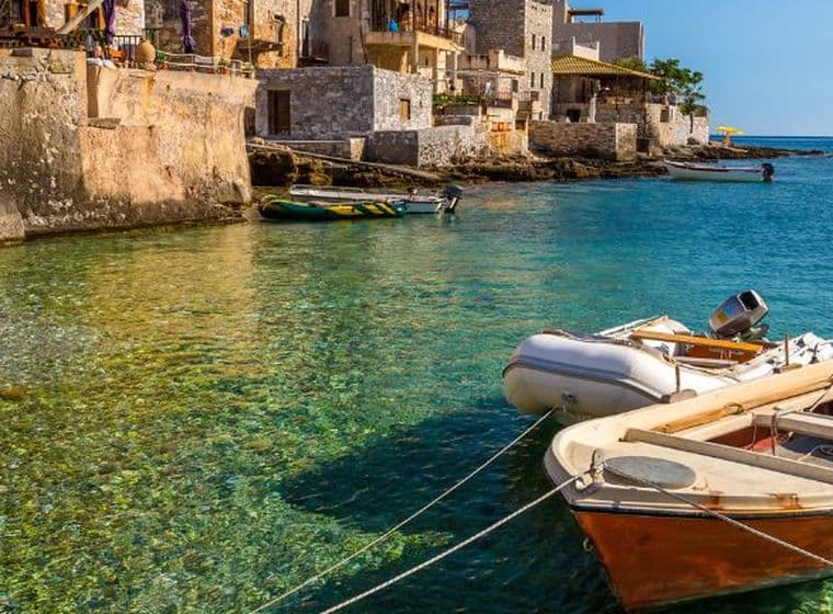 Traditional seaside village with crystal-clear turquoise waters, stone architecture, and small boats along the coast