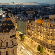 Luftaufnahme von Madrid bei Nacht, mit beleuchteten Gebäuden und verschwommenen Lichtern, die durch den fließenden Verkehr auf den Straßen verursacht werden.