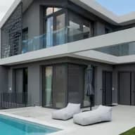 Modern two-story villa exterior with dark grey facade, swimming pool, outdoor sun loungers, glass railing balconies, and garage door