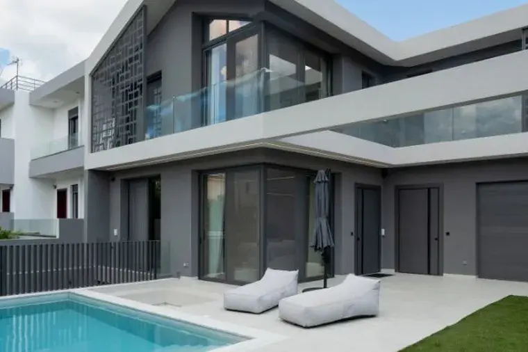 Modern two-story villa exterior with dark grey facade, swimming pool, outdoor sun loungers, glass railing balconies, and garage door