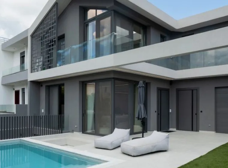 Modern two-story villa exterior with dark grey facade, swimming pool, outdoor sun loungers, glass railing balconies, and garage door