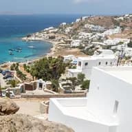 Scenic elevated view of a coastal Greek village with white whitewashed houses, turquoise bay, and rocky hillside