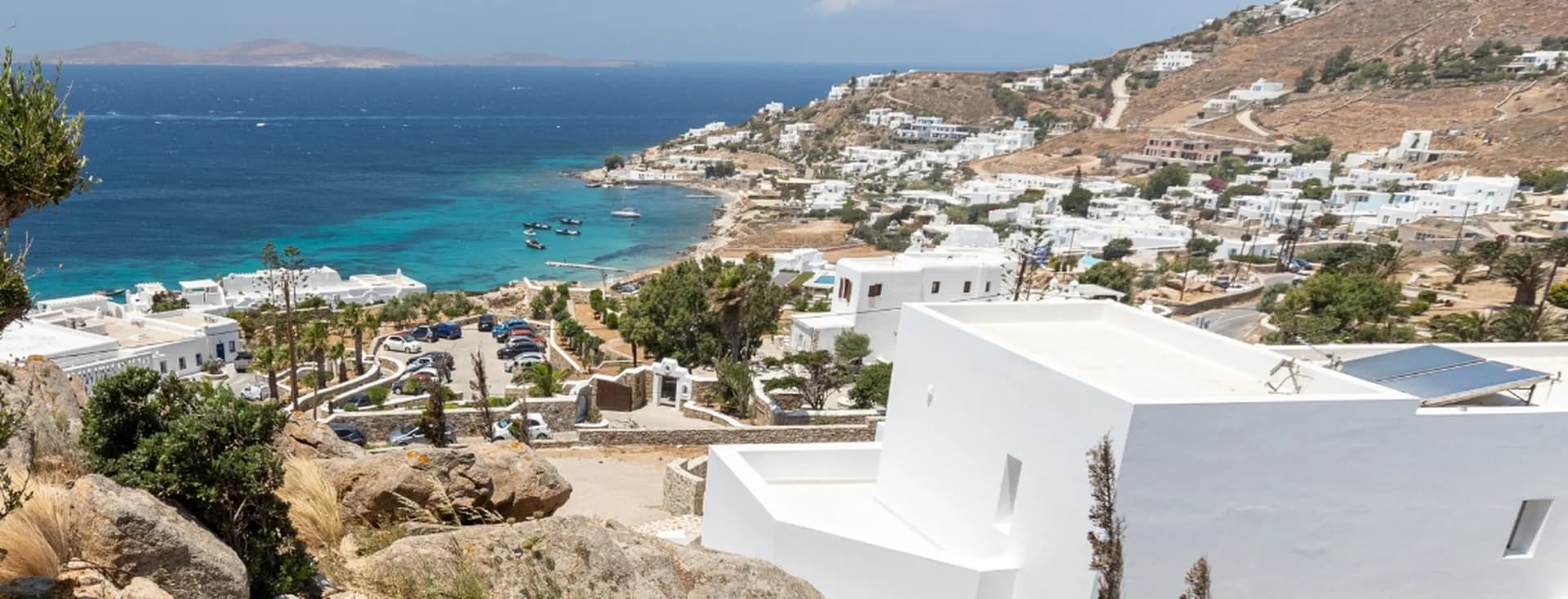 Scenic elevated view of a coastal Greek village with white whitewashed houses, turquoise bay, and rocky hillside