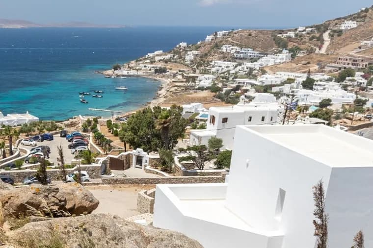 Scenic elevated view of a coastal Greek village with white whitewashed houses, turquoise bay, and rocky hillside