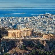 Panoramic view of Athens featuring the Acropolis, the Parthenon, and the city's coastline stretching to the Aegean Sea.