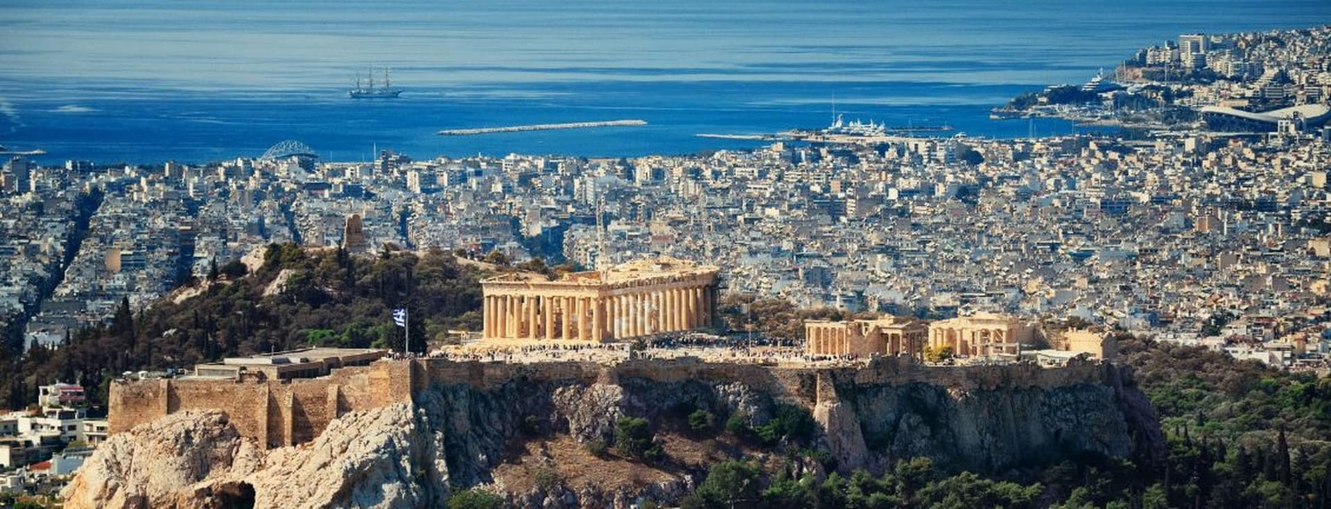 Panoramic view of Athens featuring the Acropolis, the Parthenon, and the city's coastline stretching to the Aegean Sea.