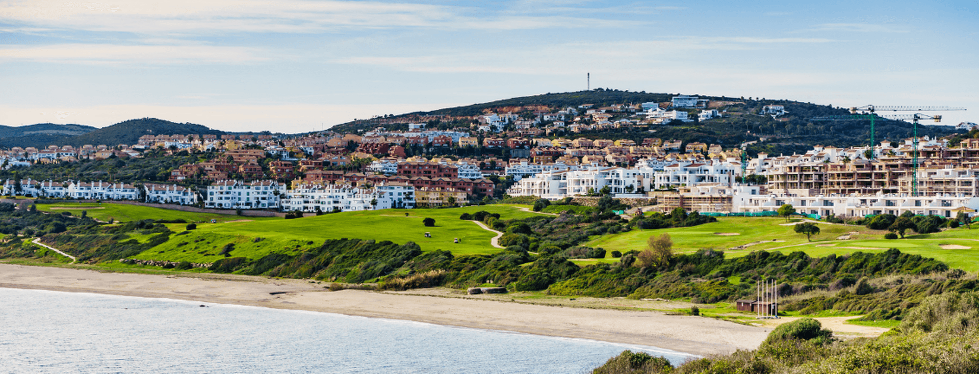 Costa de l'Alcaidesa - vista al mar, la seva platja i la urbanització. Platja en primer terme, camps verds i la urbanització al fons, de cases blanques.