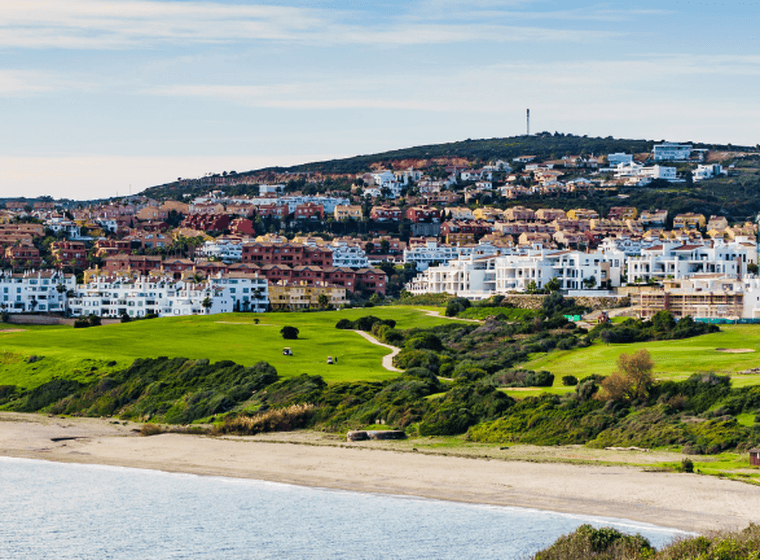 Costa de l'Alcaidesa - vista al mar, la seva platja i la urbanització. Platja en primer terme, camps verds i la urbanització al fons, de cases blanques.