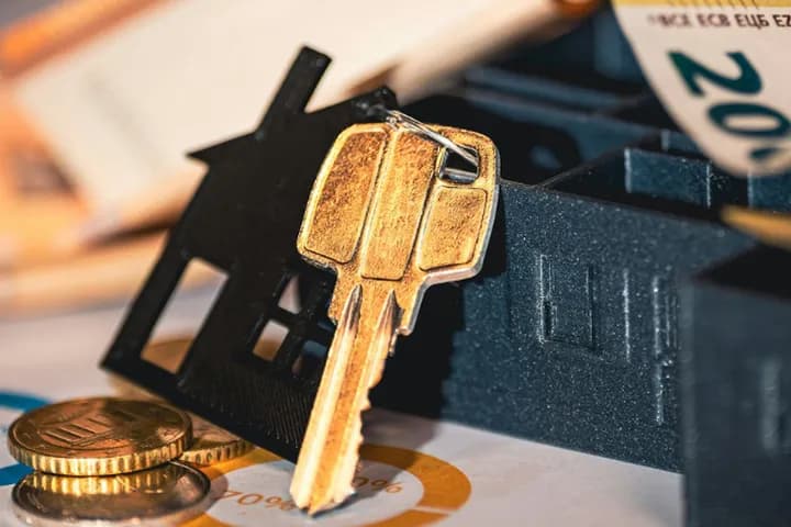 Foto zeigt einen Schlüsselhalter in Form eines schwarzen Hauses mit einem goldenen Schlüssel, Münzen und Bargeld