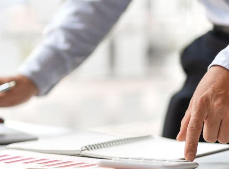 Business professional reviewing financial reports and working on a laptop in a modern office environment