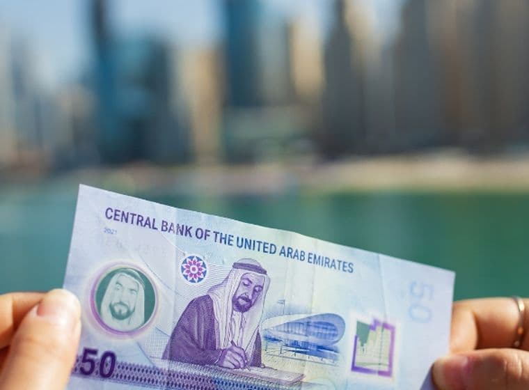 Woman holds up UAE bank note in front of Dubai skyline
