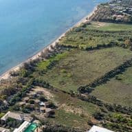Aerial view of a large beachfront plot of land along a sandy coastline with clear blue sea.