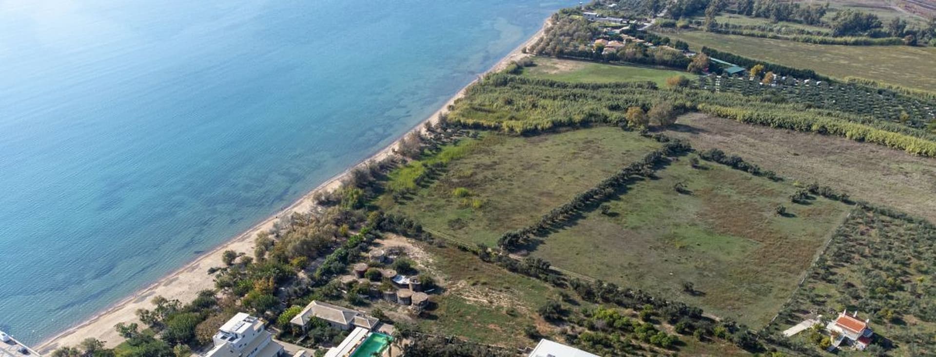 Aerial view of a large beachfront plot of land along a sandy coastline with clear blue sea.