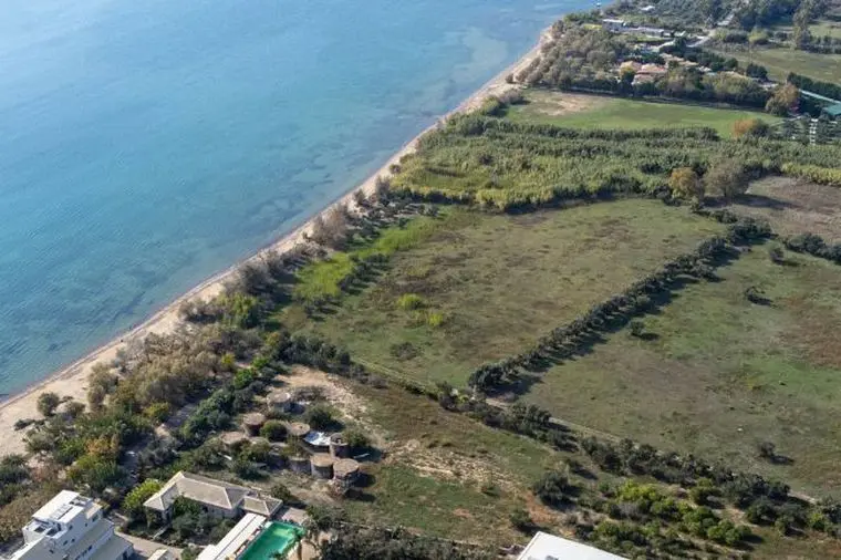Aerial view of a large beachfront plot of land along a sandy coastline with clear blue sea.