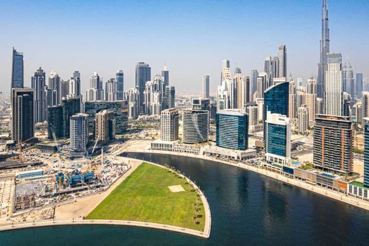 Luftaufnahme eines Kanals in Business Bay mit zahlreichen Wolkenkratzern entlang der geschwungenen Uferpromenade unter klarem blauem Himmel.