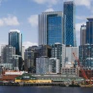 City skyline along the waterfront, featuring a large white Ferris wheel and tall glass skyscrapers against a blue sky.