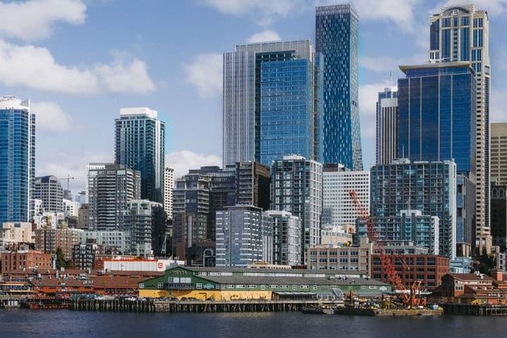 City skyline along the waterfront, featuring a large white Ferris wheel and tall glass skyscrapers against a blue sky.