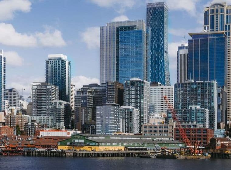 City skyline along the waterfront, featuring a large white Ferris wheel and tall glass skyscrapers against a blue sky.