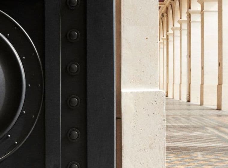 Close-up of an entrance on the left, with a background of a columned hallway featuring ornate tiled flooring on the right.