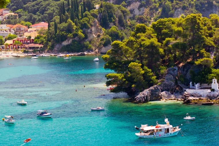 Scenic coastal bay in Parga with turquoise waters, boats, sandy beach, pine-covered islet, and white church.
