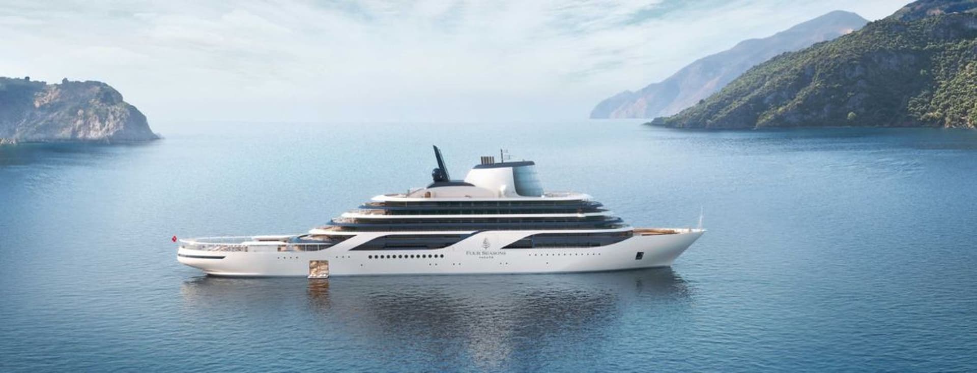 Eine weiße Luxusyacht auf dem ruhigen blauen Meer, im Hintergrund die grüne, bergige Küste.