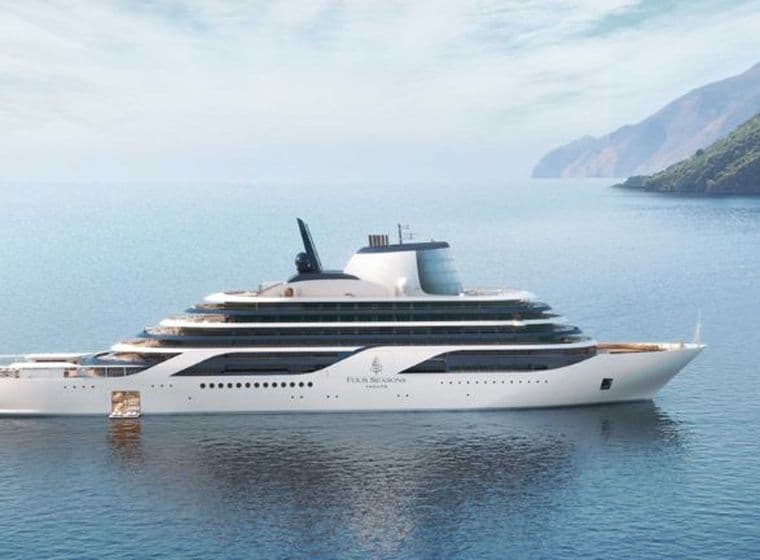 Un yacht de luxe blanc sur une mer bleue et calme, avec en arrière-plan la côte verdoyante et montagneuse.
