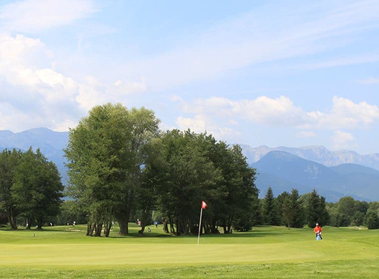 Camp de golf amb jugadors envoltat d'arbres i vistes a les muntanyes.