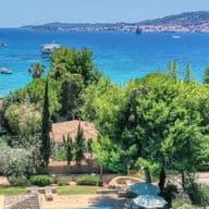 Παραθαλάσσιο τοπίο με τιρκουάζ θάλασσα, πλούσια βλάστηση και σπίτια σε λόφο με θέα στον κόλπο