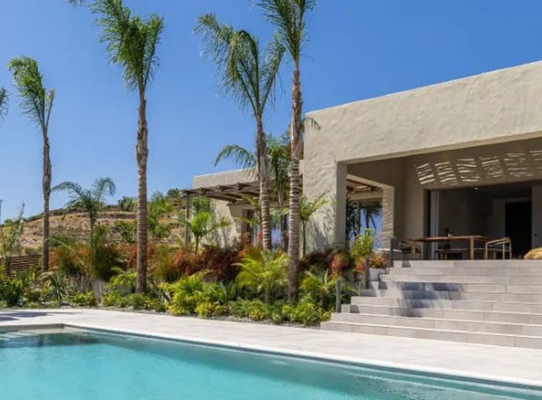 Modern luxury villa with a swimming pool, sun loungers, palm trees, and lush tropical landscaping under a clear blue sky.