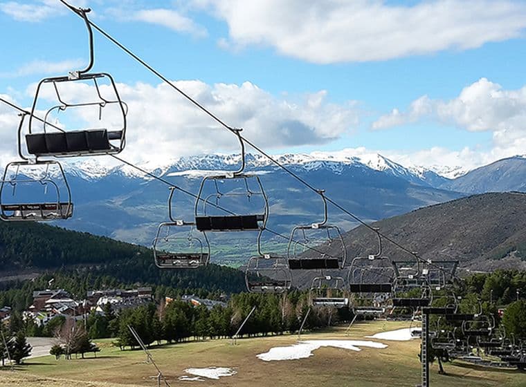 Telecadira sobre pista d’esquí a la primavera amb restes de neu, arbres i