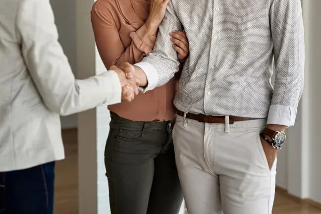 Close-up of a couple handshaking with a professional (such as a real estate agent or advisor) in a bright indoor setting.