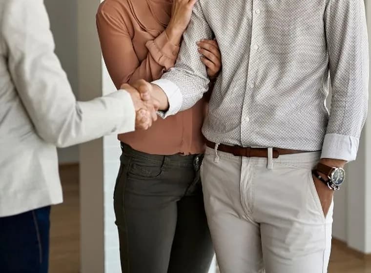 Close-up of a couple handshaking with a professional (such as a real estate agent or advisor) in a bright indoor setting.