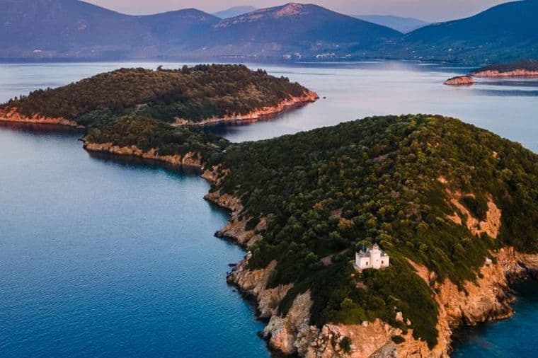 Aerial view of a long, heavily wooded peninsula with a lighthouse at the point, set against distant mountains.