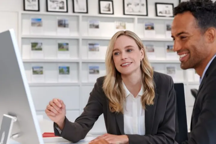 A man and a woman in business attire looking at a computer screen in an office