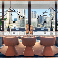 Elegant dining room in Dorchester Collection Dubai with a marble table, modern chairs, large windows showcasing a cityscape, and vibrant decor with plants and warm lighting.