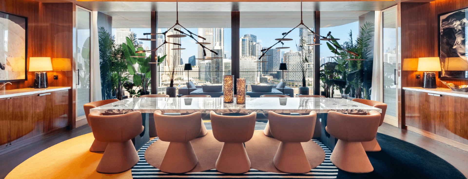 Elegant dining room in Dorchester Collection Dubai with a marble table, modern chairs, large windows showcasing a cityscape, and vibrant decor with plants and warm lighting.