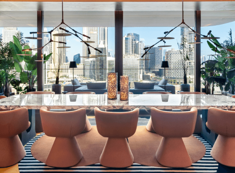 Elegant dining room in Dorchester Collection Dubai with a marble table, modern chairs, large windows showcasing a cityscape, and vibrant decor with plants and warm lighting.