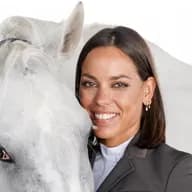 Portrait of a female equestrian wearing a riding helmet and vest, looking attentively into the distance.