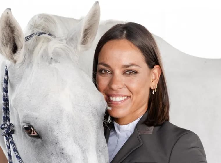 Portrait of a female equestrian wearing a riding helmet and vest, looking attentively into the distance.