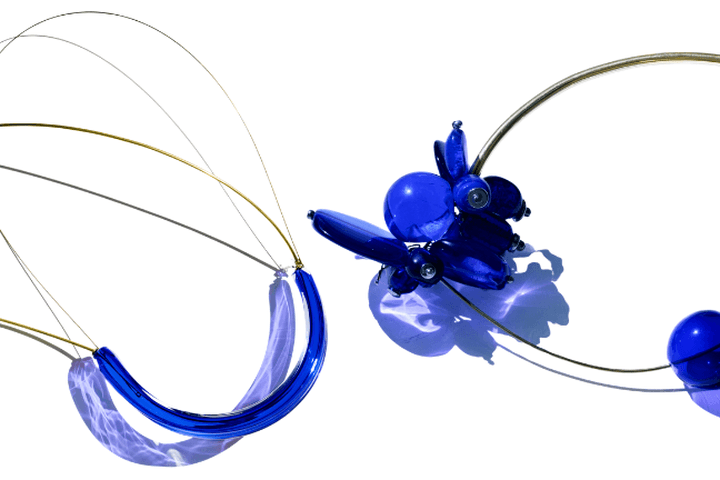 Dos esculturas abstractas de cristal con cuentas de color azul cobalto, unidas entre sí por finos hilos, sobre un fondo blanco.
